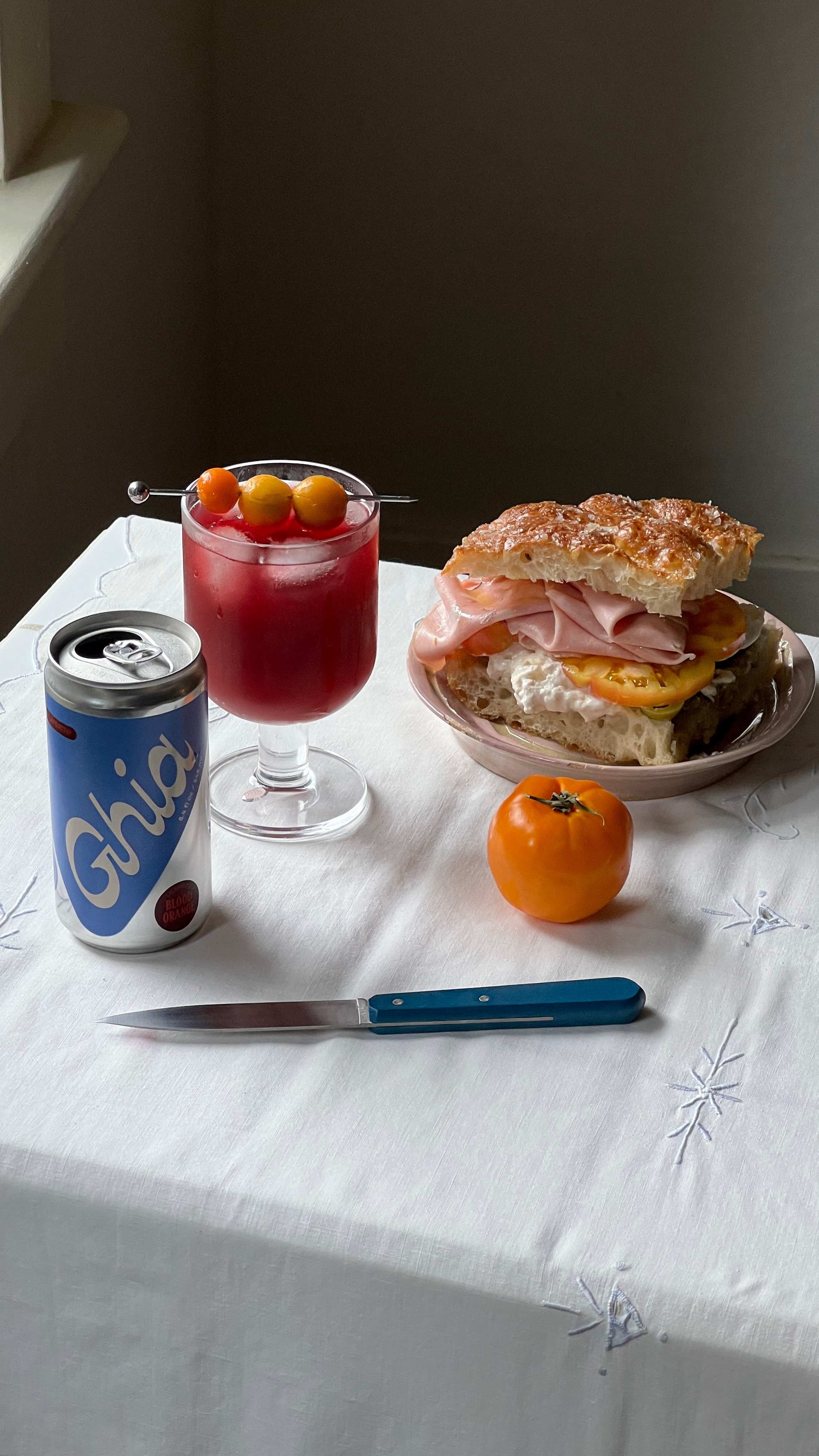 Ghia Spritz in a glass paired with a Mortadella sandwich on a white table cloth