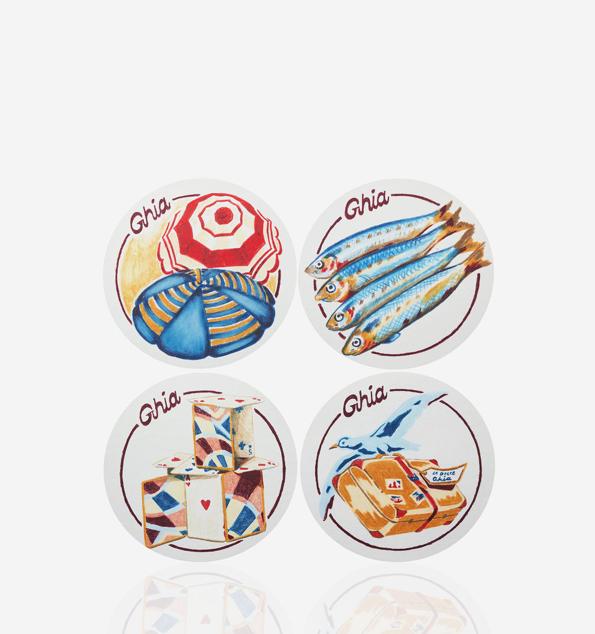 Four round Ghia coasters with illustrated designs featuring a beach umbrella, fish, stacked playing cards, and a suitcase with a bird.