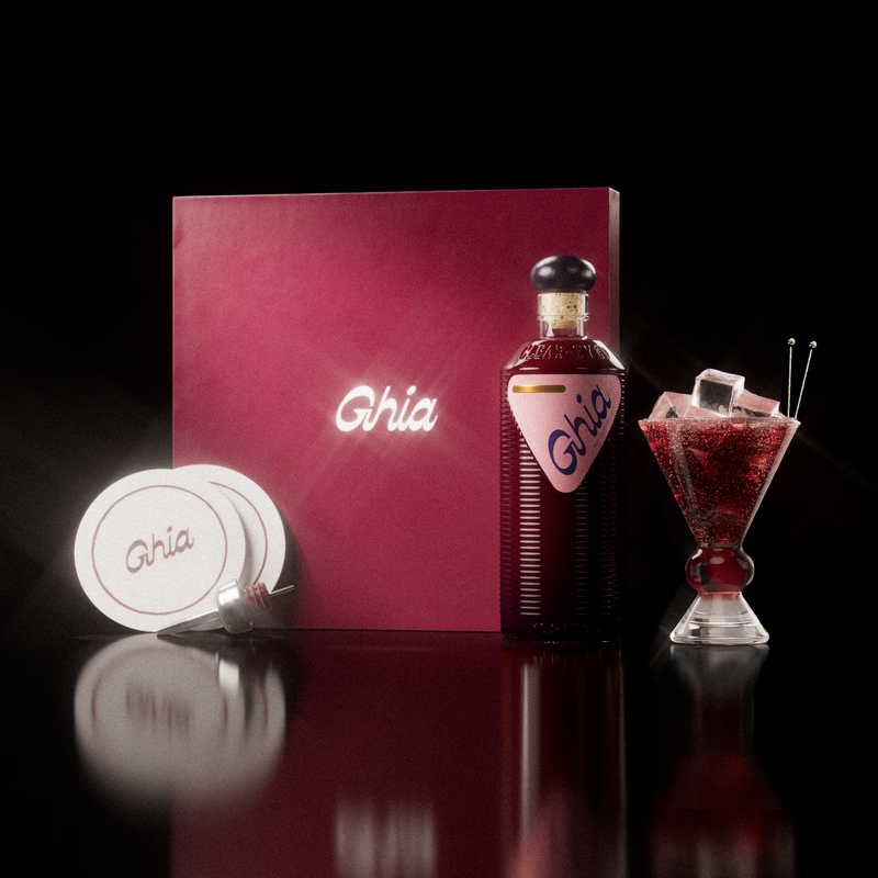 A Ghia non-alcoholic aperitif gift set with a burgundy box, paper coasters, 1 glass bottle of Berry Apéritif, and a decorative cocktail glass that has a amber and clear base.