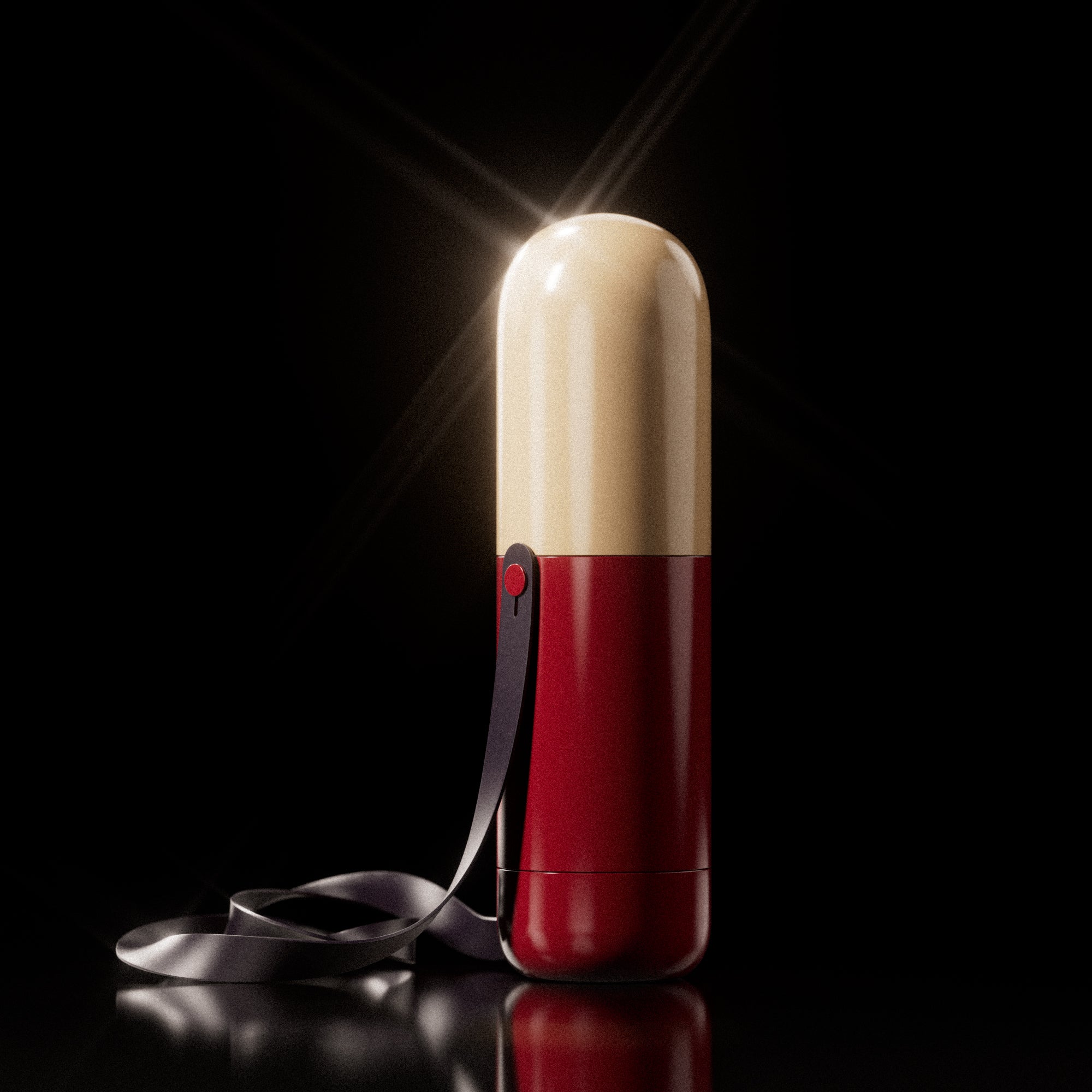 A capsule-shaped Ghia container in red and cream with a black strap, standing upright against a black background with a spotlight.