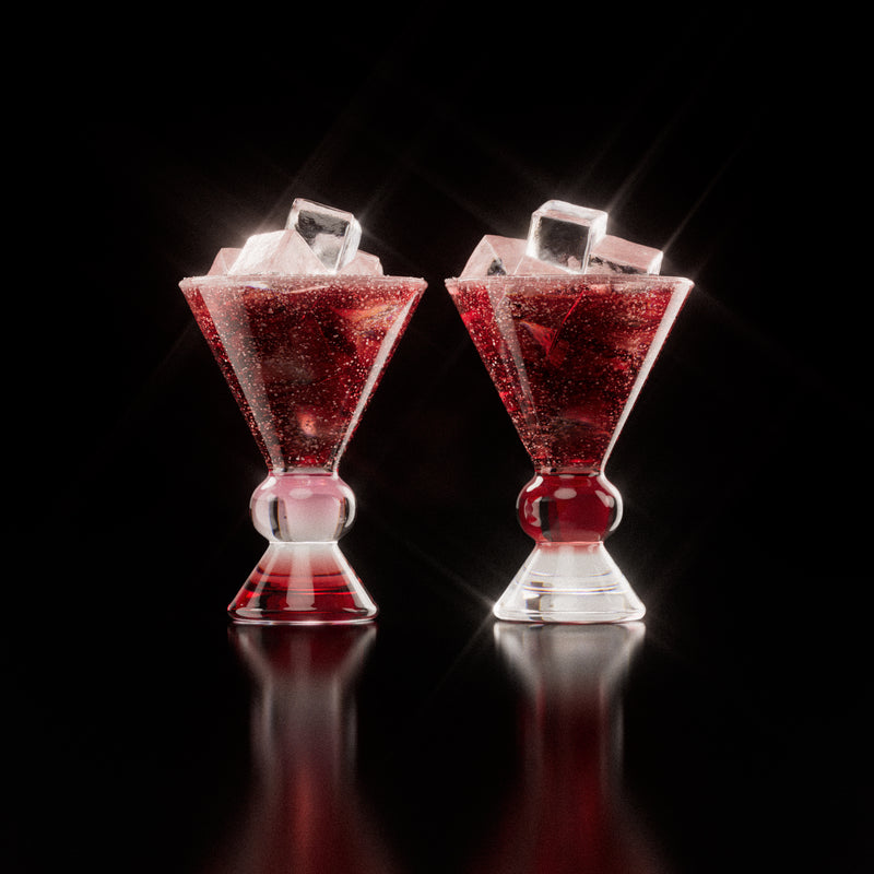 Two decorative glasses that have a red and clear base, each containing a red drink with ice cubes, highlighting the distinctive totem-inspired shape of the glasses against a light background.