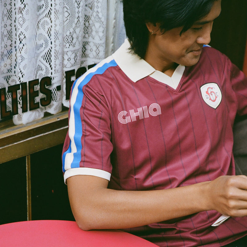 Man seated at a red table wearing the maroon Ghia Jersey with retro GHIA lettering