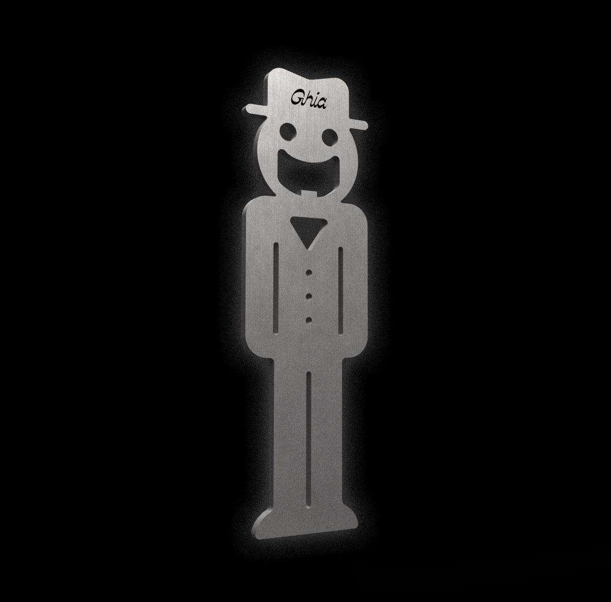 A Ghia-branded metal figure with a smiling face, hat, and buttoned outfit, crafted from brushed stainless steel.