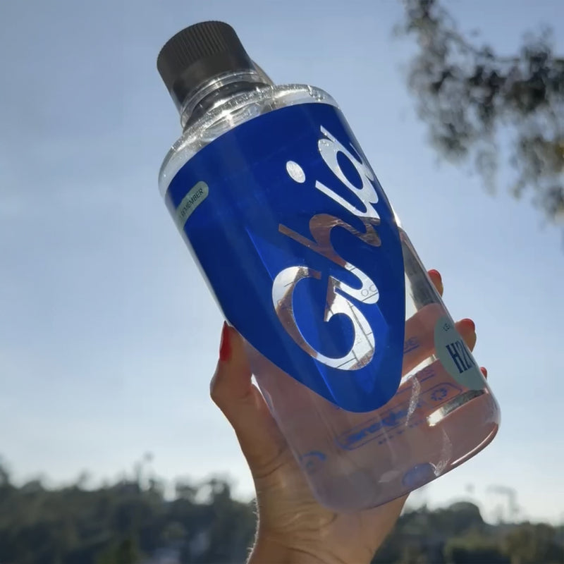 A clear plastic water bottle with the words 'GHIA' on a blue label, held up against the sky.