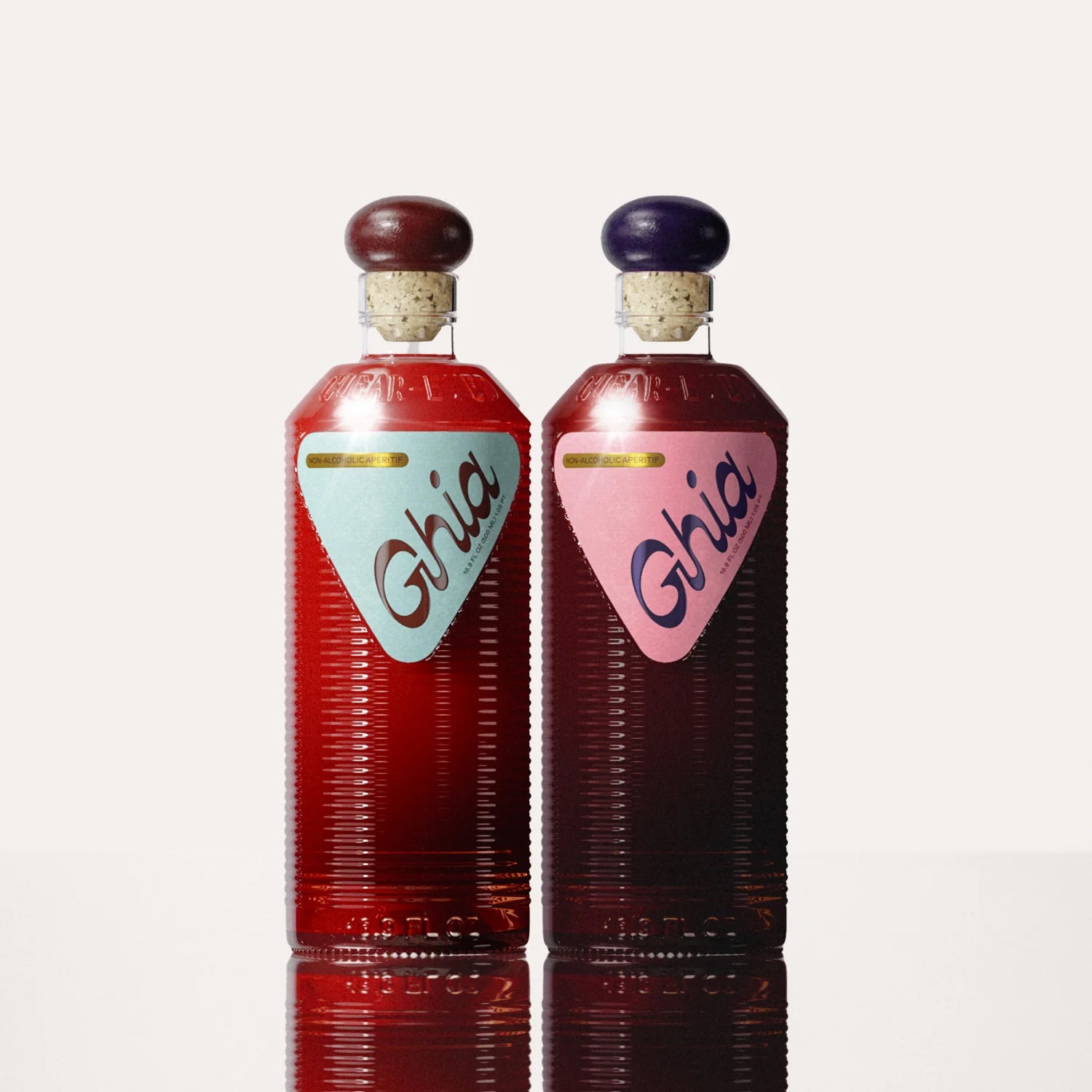 Two non-alcoholic beverages in Berry Apéritif & Original bottles with ribbed glass, cork tops, and bold branding; one with a light blue label on the left, the other with a pink label on the right.