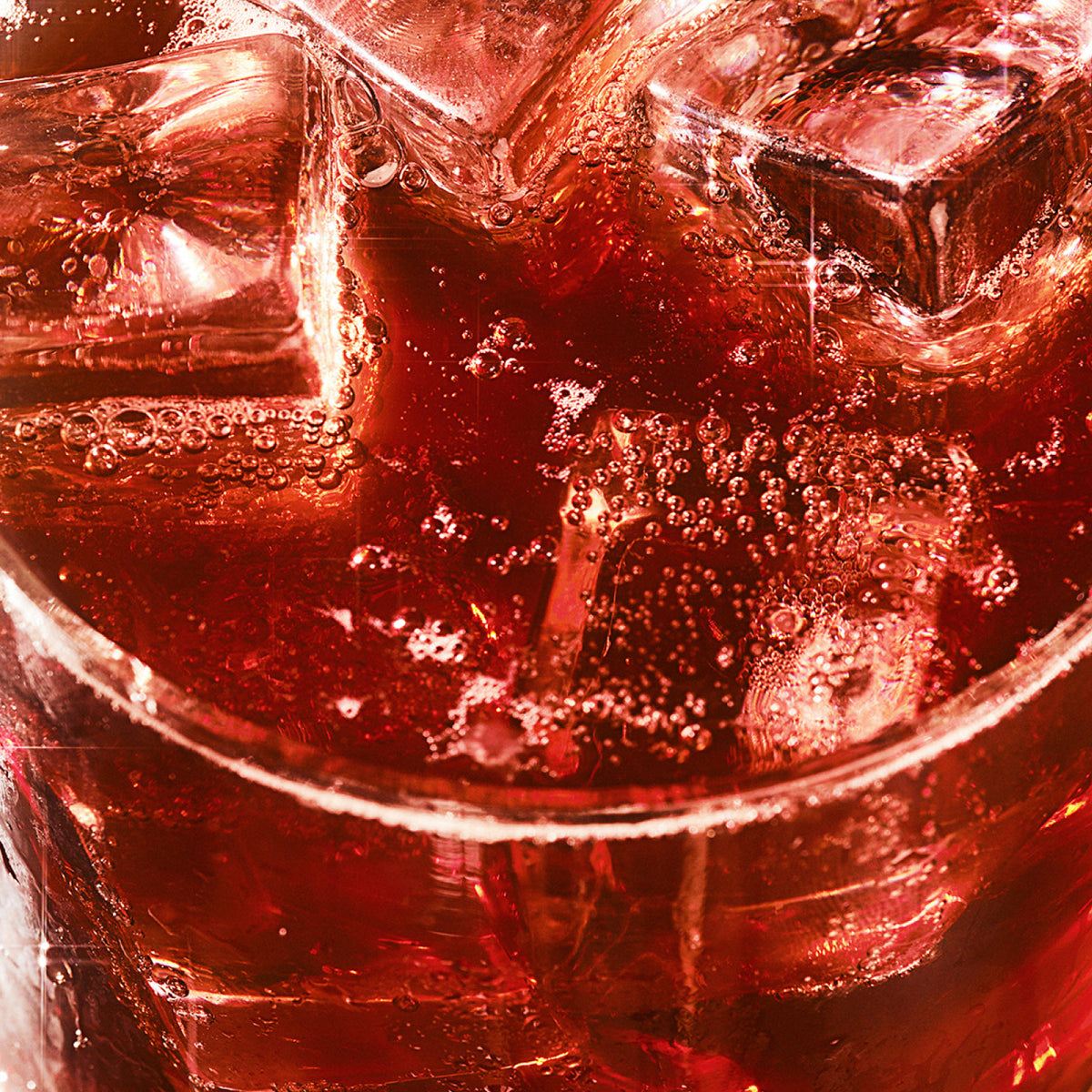 Close-up of a drink with ice cubes, bubbles, and a deep red color, likely showcasing a Ghia non-alcoholic aperitif in a glass.