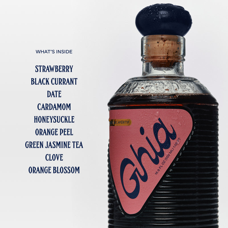 A bottle of Ghia non-alcoholic aperitif with a list of ingredients beside it: strawberry, black currant, date, cardamom, and more. The bottle has a pink label with the word "Ghia.