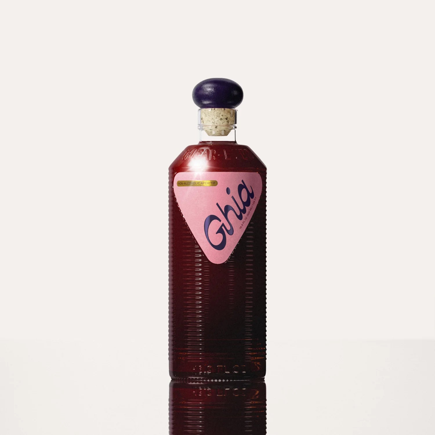 A Ghia non-alcoholic beverage in flavor Berry Apéritif clear bottle with ribbed glass, a purple cork top, and a pink label featuring bold branding on a reflective surface.