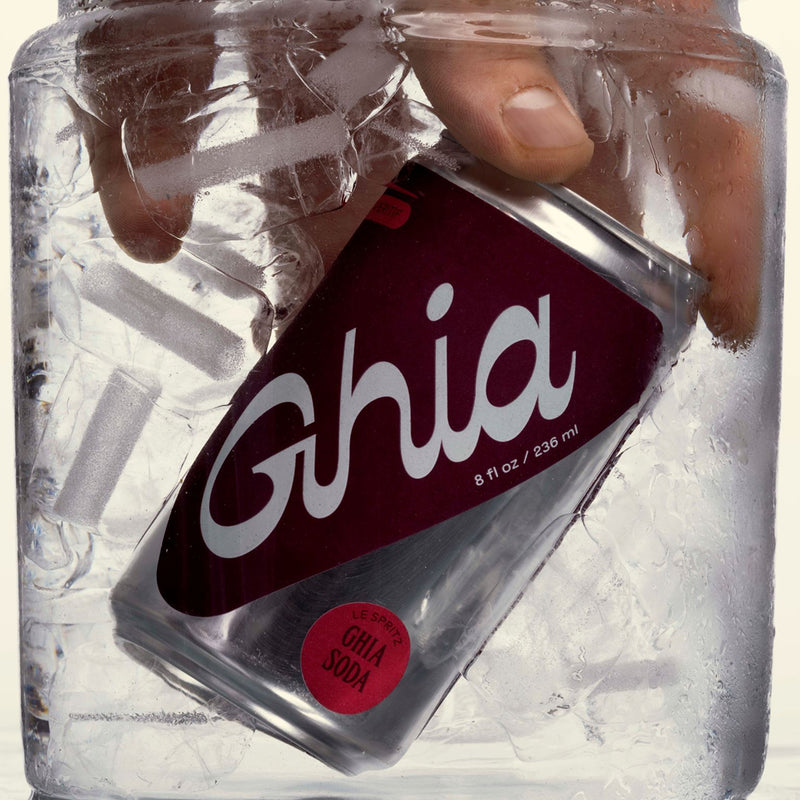 A hand reaching into a block of ice to grab a can of Ghia Soda non-alcoholic spritz, partially submerged in the ice, with condensation on the can.