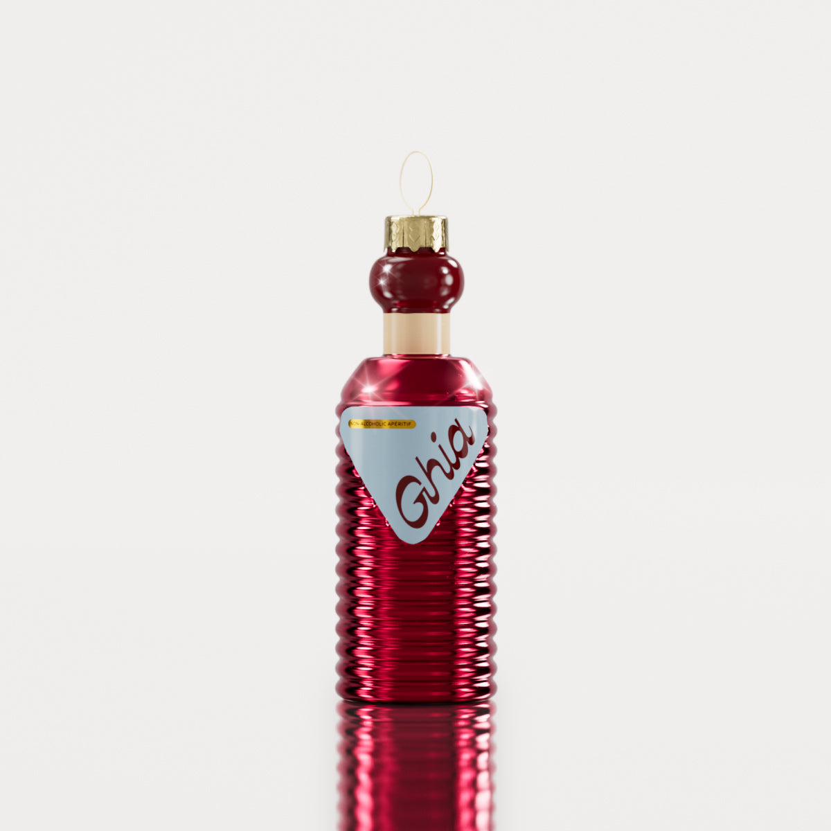 A Ghia-themed holiday ornament shaped like a ribbed glass bottle with a red metallic finish, a blue label, and a gold hanging loop.