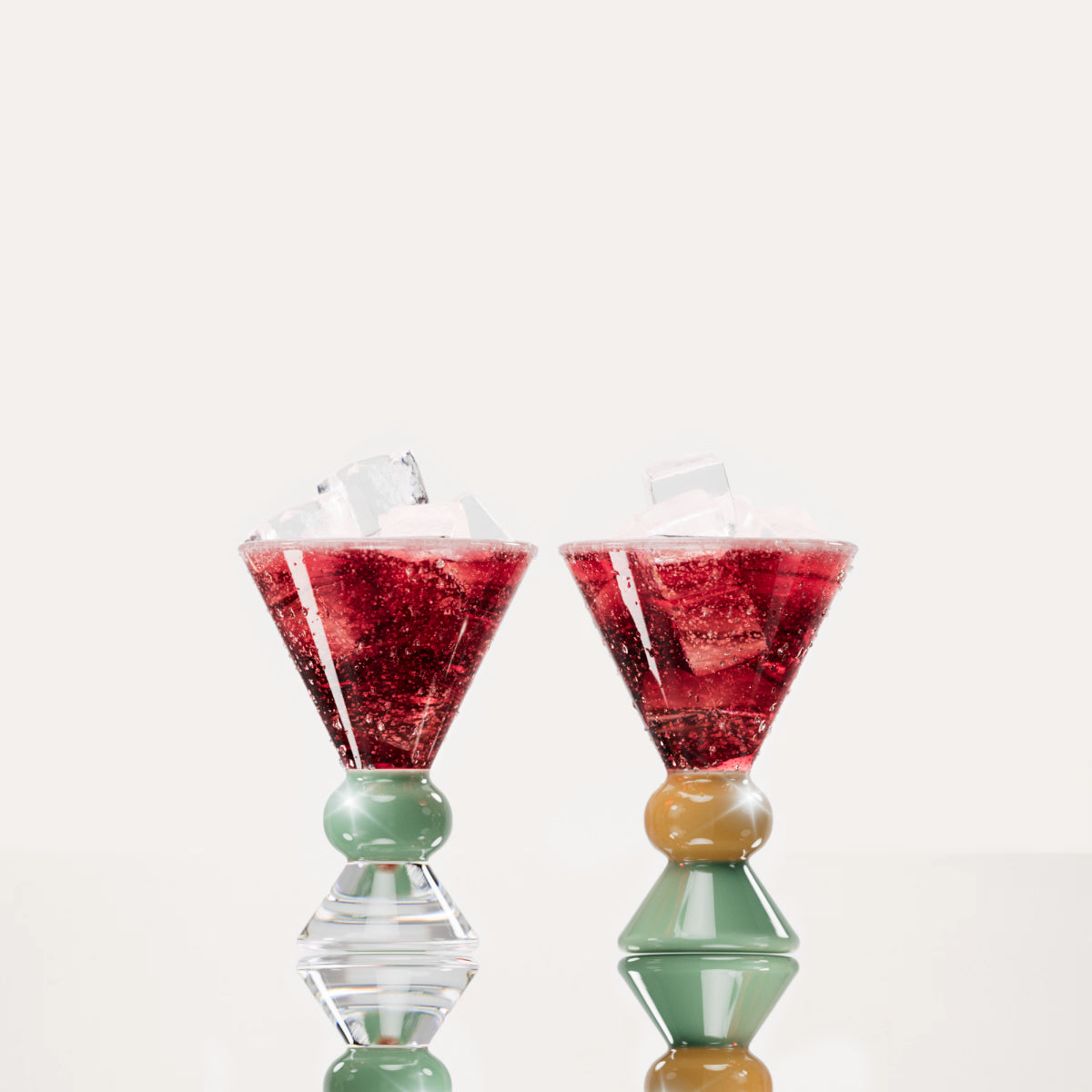 Two decorative glasses, each containing a red drink with ice cubes, highlighting the distinctive totem-inspired shape of the glasses against a light background with a clear, jade and sand base.