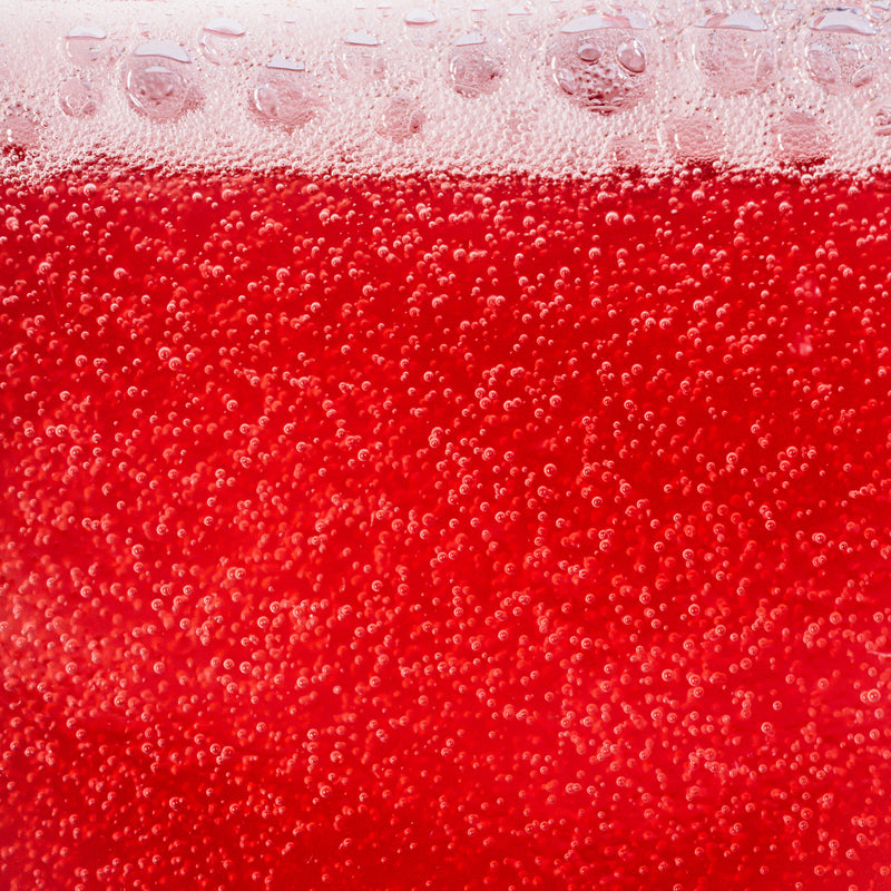 Close-up of a red, bubbly beverage with small bubbles rising to the surface, likely showcasing a Ghia non-alcoholic aperitif in a glass.
