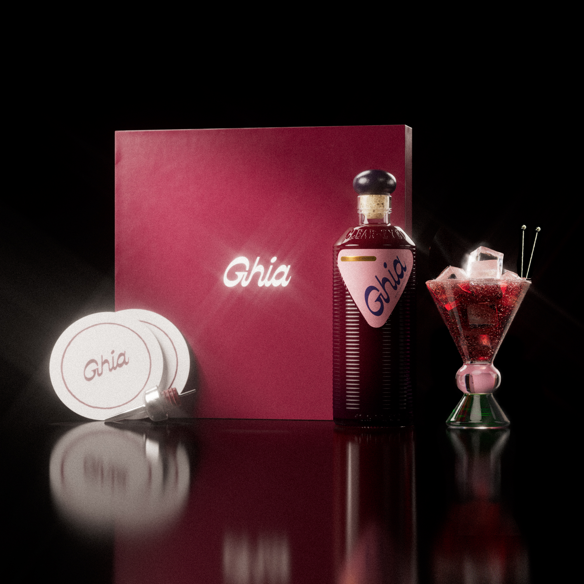 A Ghia non-alcoholic aperitif gift set with a burgundy box, paper coasters, 1 glass bottle of Berry Apéritif, and a decorative cocktail glass that has a pink and green base.