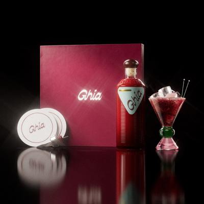 A Ghia non-alcoholic aperitif gift set with a burgundy box, paper coasters, 1 glass bottle of Original Apéritif, and a decorative cocktail glass that has a green and pink base.