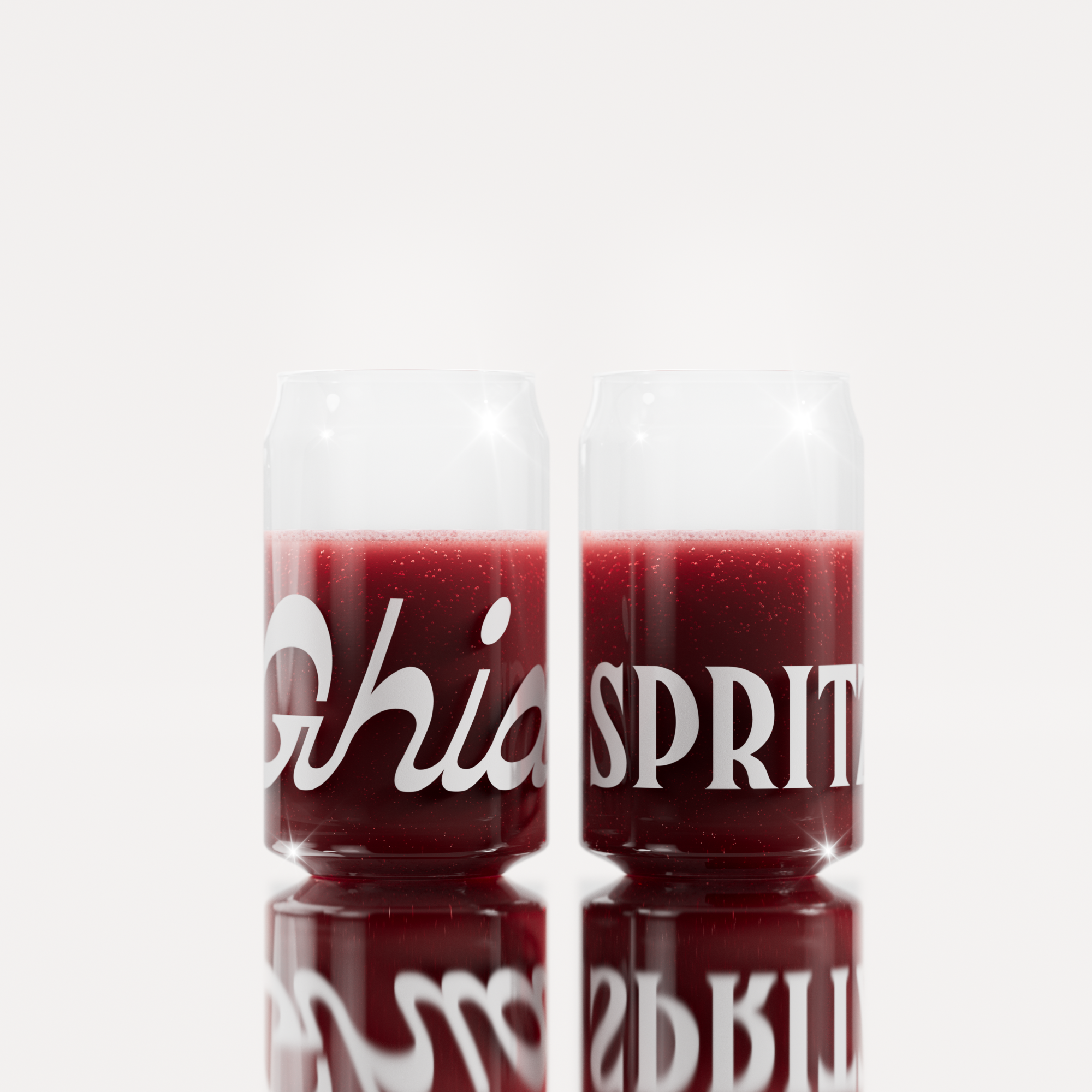 Two clear Ghia-branded glasses filled with a deep red sparkling beverage, featuring bold white lettering wrapping around the surface.