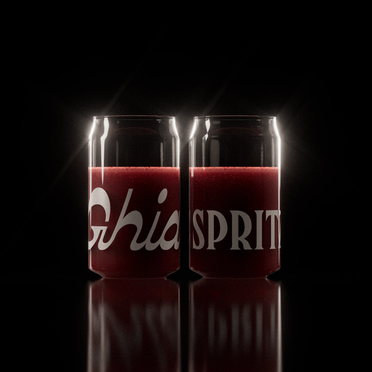 Two clear Ghia-branded glasses filled with a deep red sparkling beverage, featuring bold white lettering wrapping around the surface.