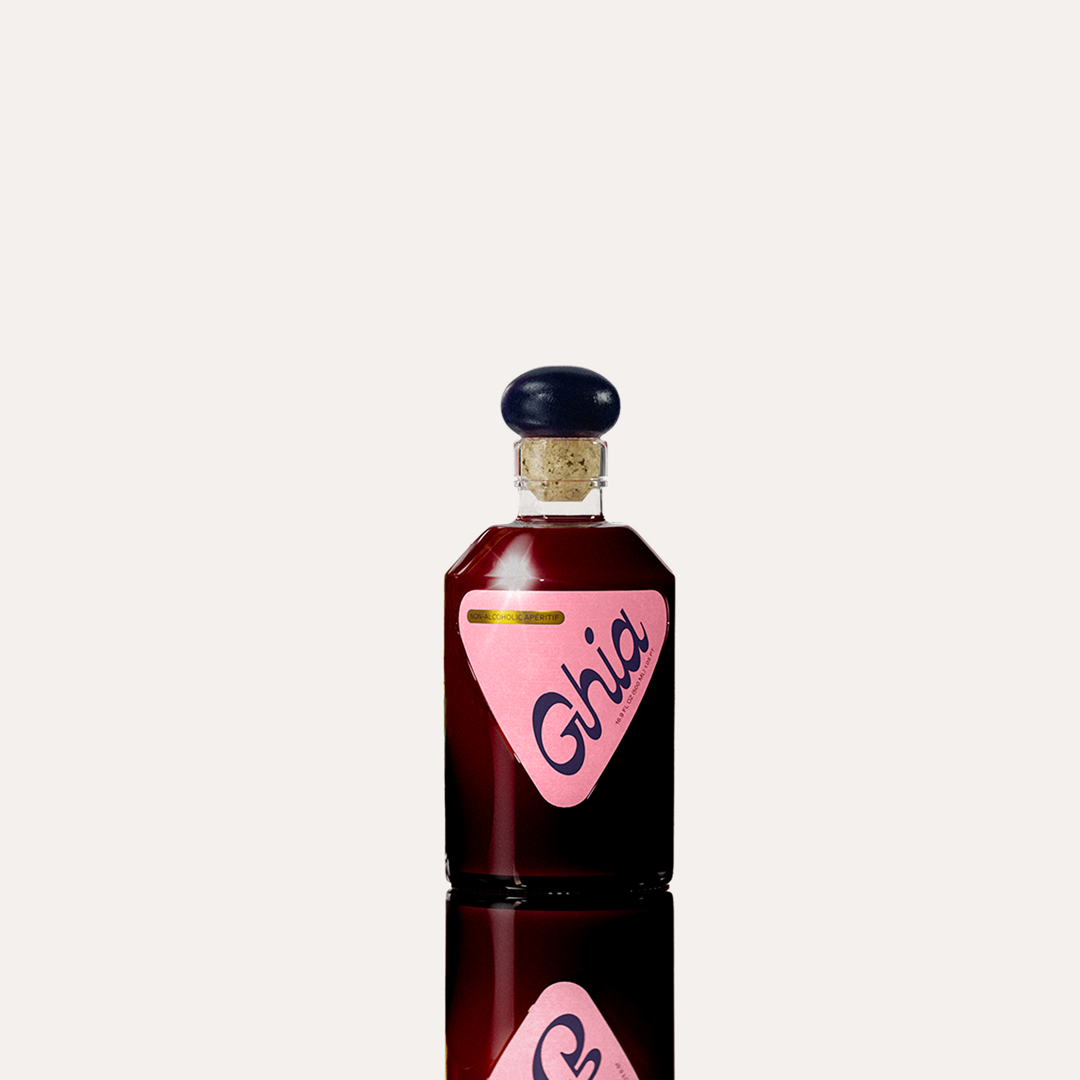 A Ghia non-alcoholic beverage in flavor Berry Apéritif clear bottle a purple cork top, and a pink label featuring bold branding on a reflective surface.