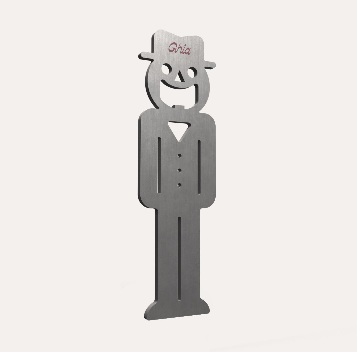 A Ghia-branded metal figure with a smiling face, hat, and buttoned outfit, crafted from brushed stainless steel.