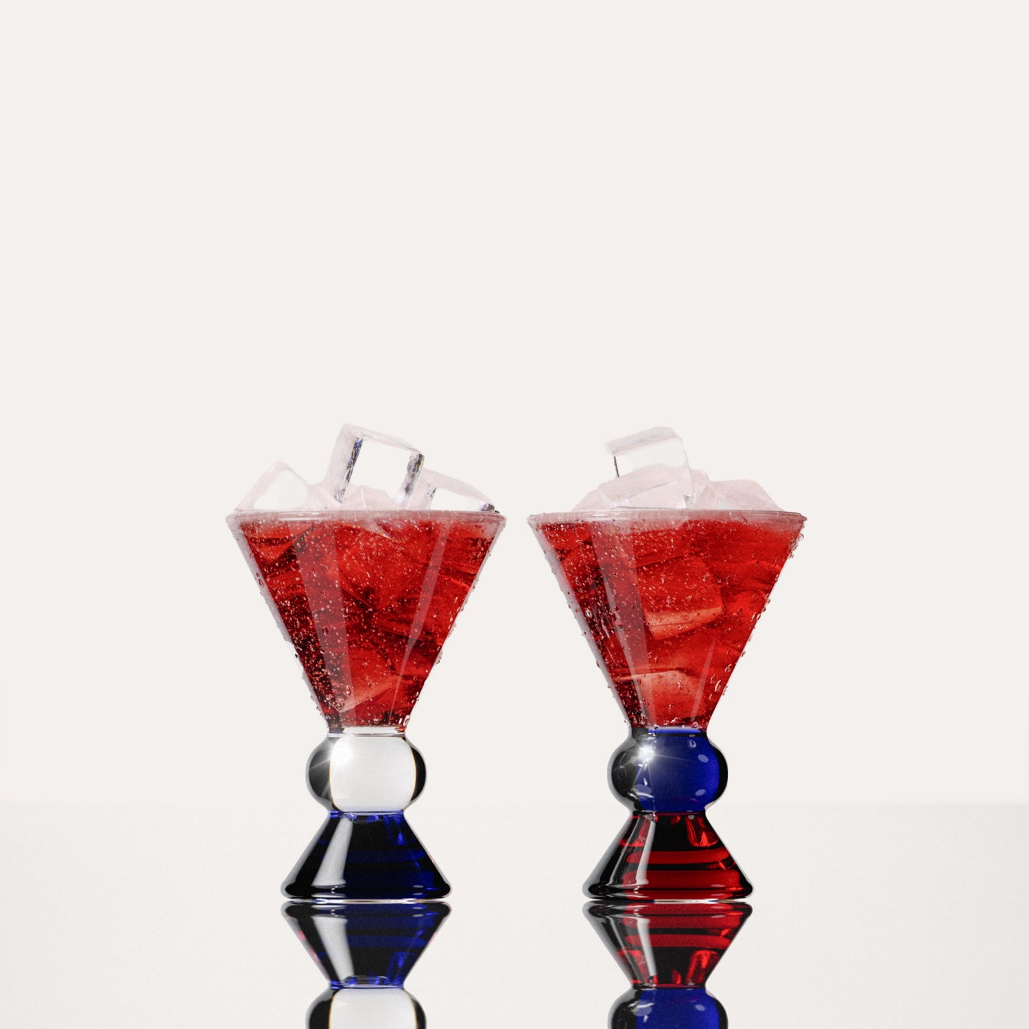 Two decorative glasses that have an amber, clear and blue base, each containing a red drink with ice cubes, highlighting the distinctive totem-inspired shape of the glasses against a light background.