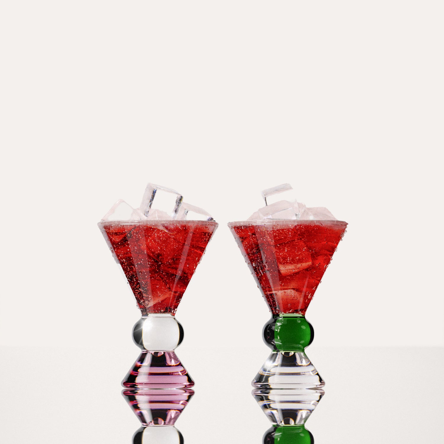 Two decorative glasses that have a pink, clear and green base, each containing a red drink with ice cubes, highlighting the distinctive totem-inspired shape of the glasses against a light background.