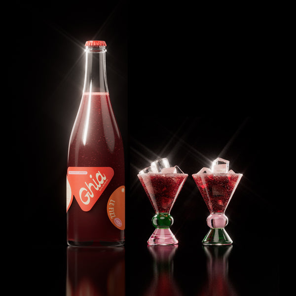 Non-alcoholic spritz in a bottle filled with a deep red strawberry and orange blossom beverage, featuring red labels. Alongside decorative cocktail glass that has a green and pink base.