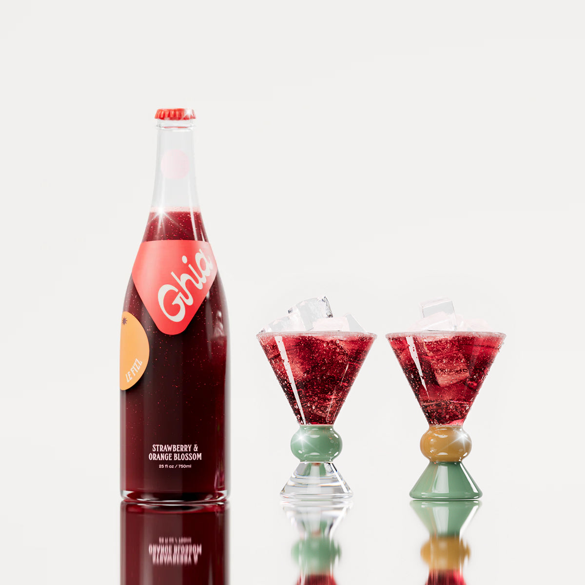 Non-alcoholic spritz in a bottle filled with a deep red strawberry and orange blossom beverage, featuring red labels. Alongside decorative cocktail glass that has a clear, jade and sand base.