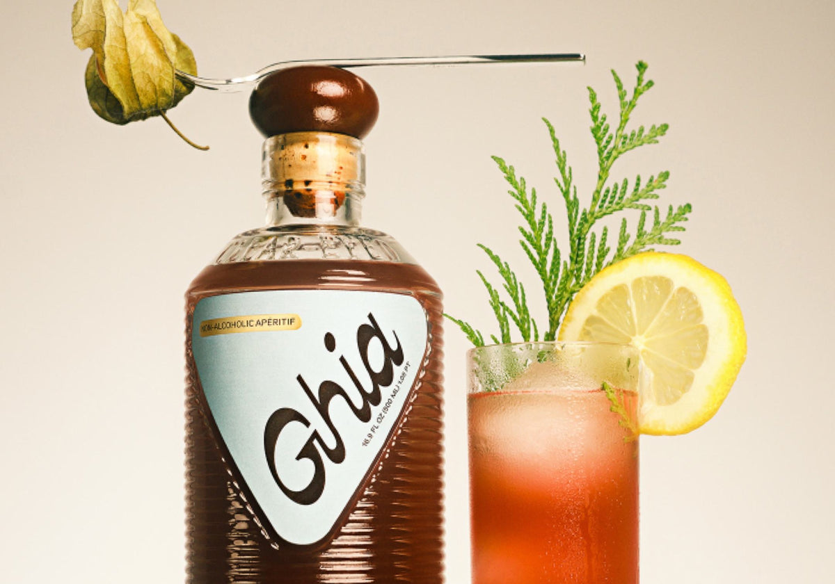 Ghia non-alcoholic apéritif bottle beside a spritz garnished with lemon and greenery